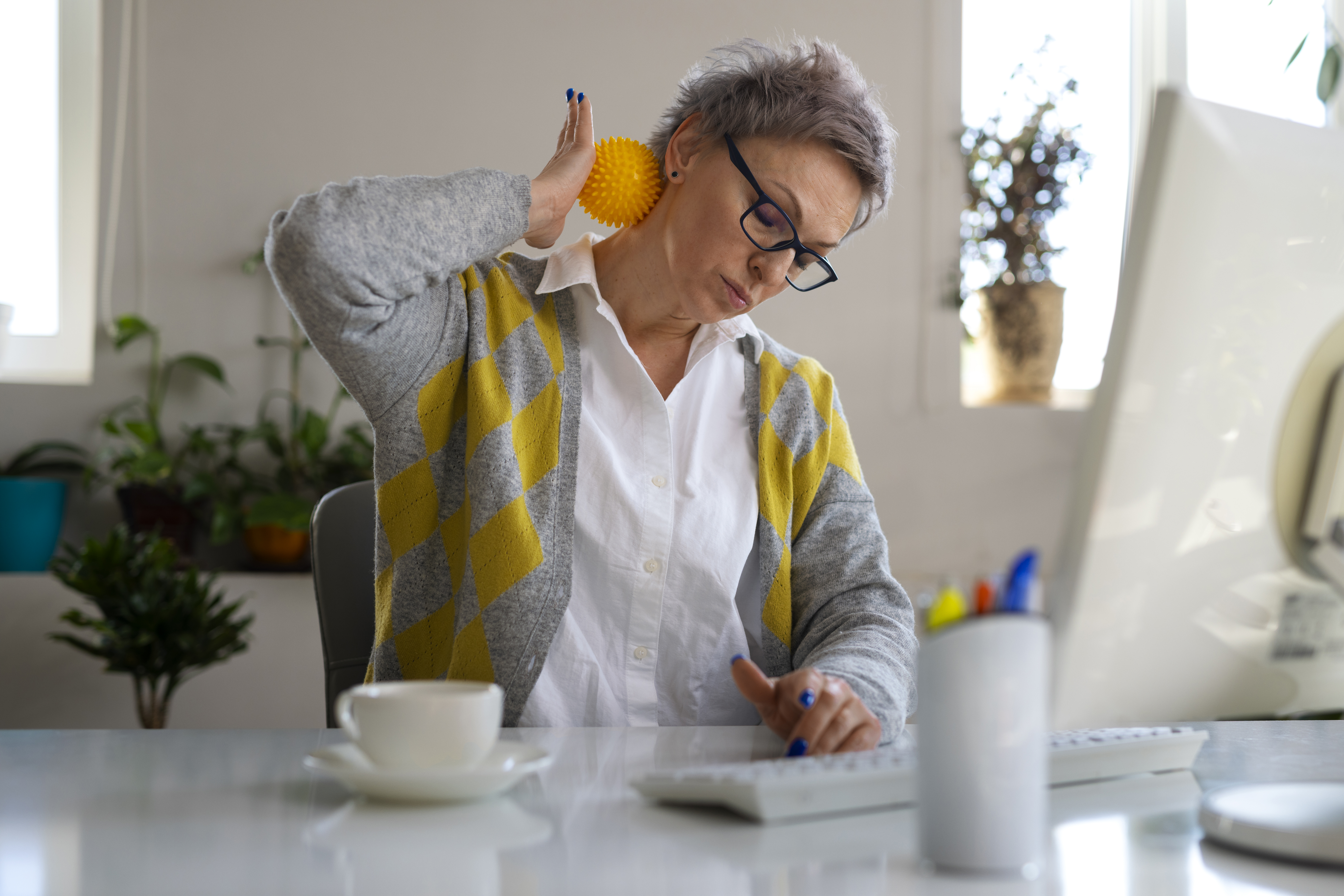 Person sitting at a work desk, massaging their neck.