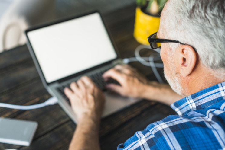 Photograph of an older person wearing glasses and working on their laptop.