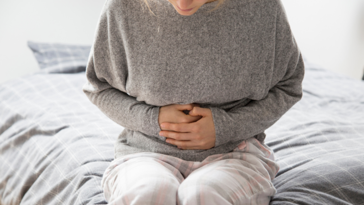 A person sat on the edge of the bed holding their stomach in pain.