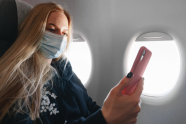 photograph of a person sat on an aeroplane with a face mask covering their nose and mouth.