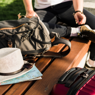 A person sat on a bench with a rucksack, hat and map placed next to them.